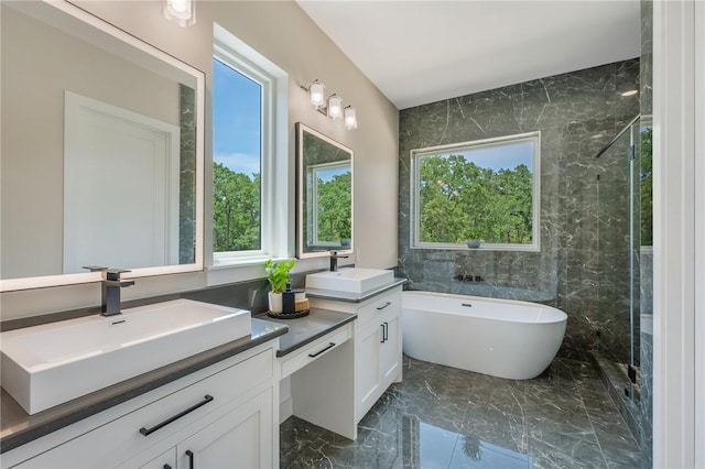 bathroom with marble tiled flooring, healthy amount of natural light, a soaking tub, and two vanities