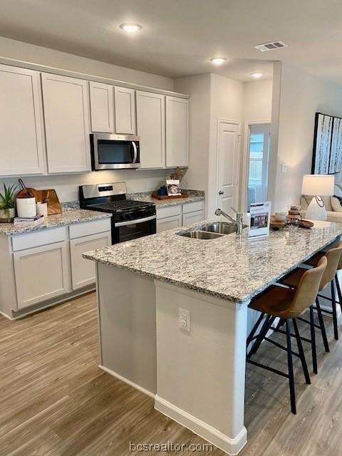 kitchen featuring sink, stainless steel appliances, a kitchen island with sink, white cabinets, and light wood-type flooring