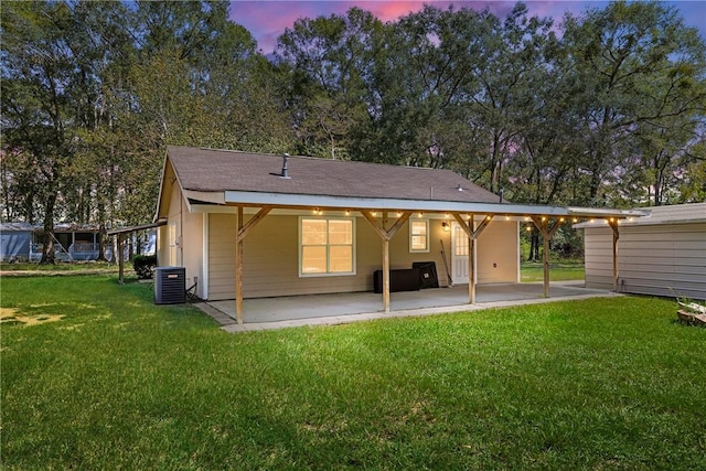 back house at dusk featuring a lawn, central AC unit, and a patio area