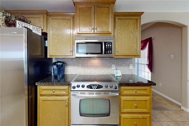 kitchen with dark stone countertops, backsplash, light tile patterned floors, and stainless steel appliances