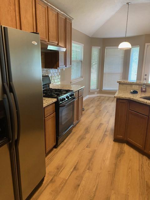 2704 Barronwood Dr, Bryan, TX 77807 - kitchen featuring stainless steel fridge with ice dispenser, black gas range, under cabinet range hood, brown cabinets, and lofted ceiling