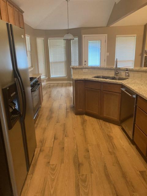 2704 Barronwood Dr, Bryan, TX 77807 - kitchen with stainless steel appliances, a sink, light wood-style floors, brown cabinets, and light stone counters