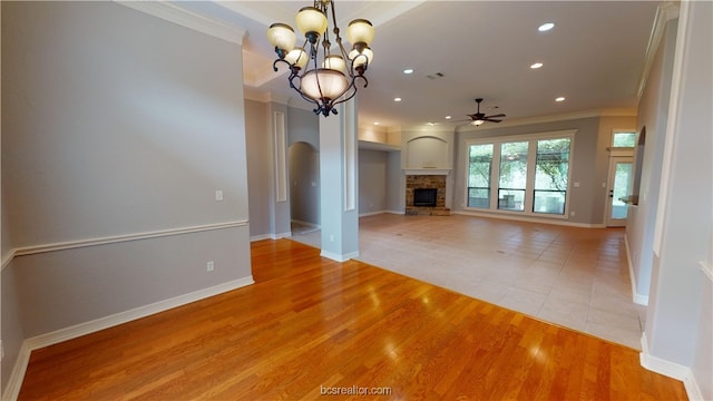 unfurnished living room featuring a stone fireplace, light hardwood / wood-style flooring, ceiling fan with notable chandelier, and ornamental molding