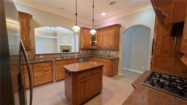 kitchen featuring appliances with stainless steel finishes, a sink, arched walkways, brown cabinetry, and crown molding