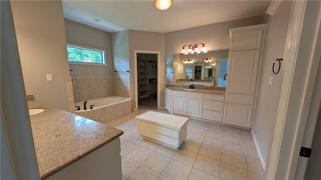 full bathroom with two vanities, tile patterned floors, a bath, a walk in closet, and baseboards