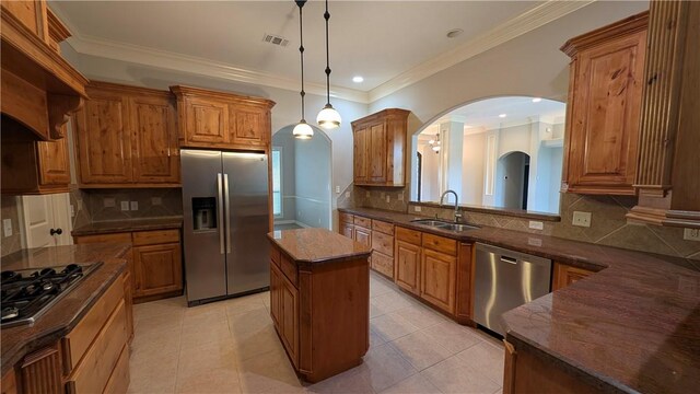 kitchen featuring stainless steel appliances, a sink, arched walkways, a kitchen island, and brown cabinetry