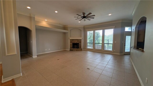unfurnished living room featuring crown molding, arched walkways, a ceiling fan, baseboards, and light tile patterned floors