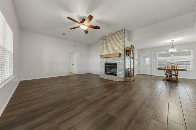 unfurnished living room featuring baseboards, dark wood-style floors, a fireplace, and ceiling fan with notable chandelier