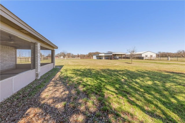 view of yard with a rural view, fence, and a sunroom