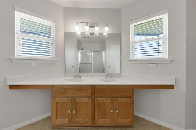 bathroom featuring a shower stall, double vanity, baseboards, and a sink