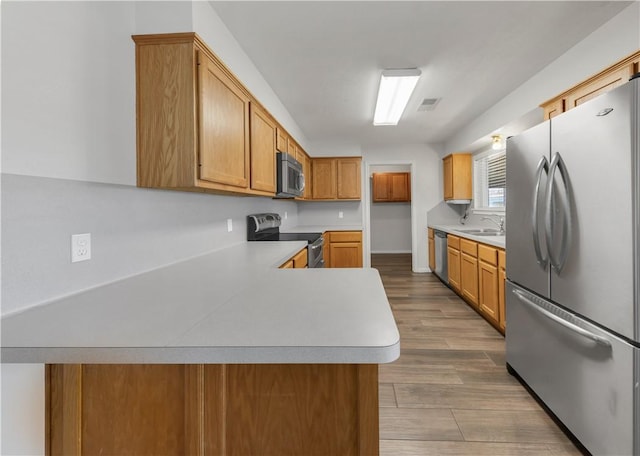 kitchen featuring a sink, stainless steel appliances, wood finished floors, and light countertops