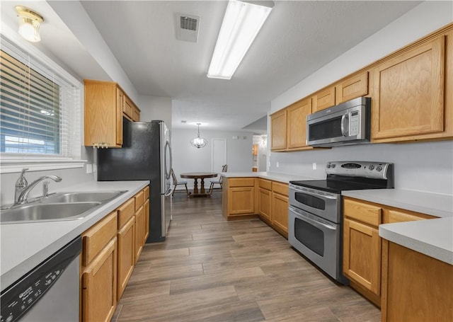 kitchen featuring visible vents, appliances with stainless steel finishes, a peninsula, wood finished floors, and a sink