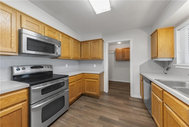 kitchen featuring baseboards, dark wood finished floors, light countertops, stainless steel appliances, and a sink