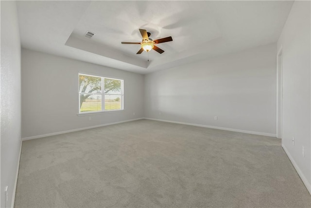 unfurnished room with visible vents, a ceiling fan, a tray ceiling, baseboards, and light colored carpet