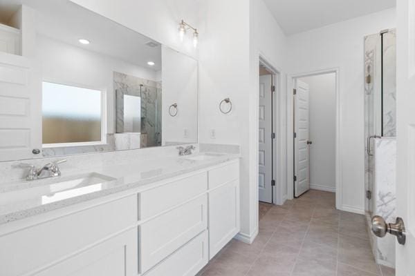 full bath with double vanity, a sink, a marble finish shower, and tile patterned flooring