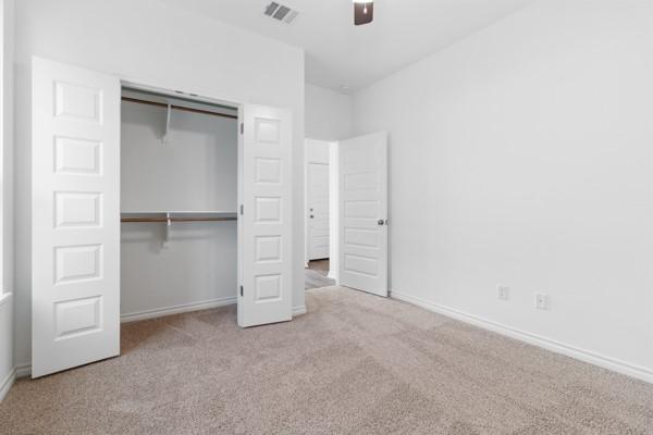 unfurnished bedroom featuring a ceiling fan, visible vents, baseboards, a closet, and carpet flooring