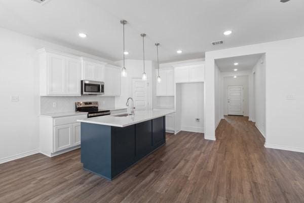 kitchen with an island with sink, stainless steel appliances, white cabinetry, and dark wood-type flooring