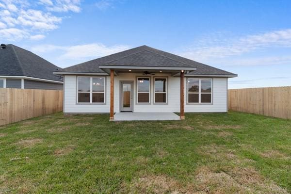 back of property with a ceiling fan, roof with shingles, a patio area, a fenced backyard, and a yard