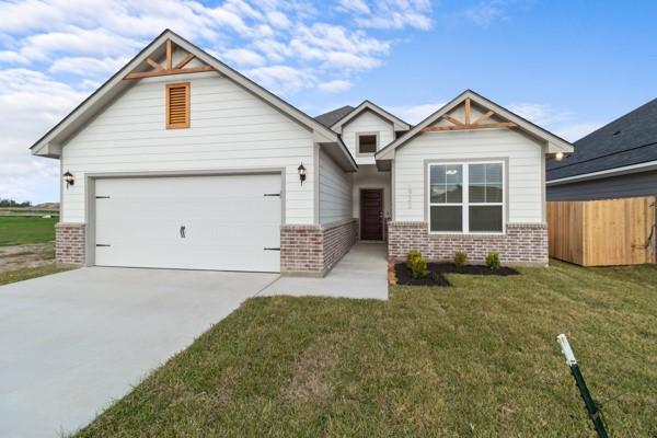 craftsman-style house featuring fence, a front yard, brick siding, an attached garage, and driveway