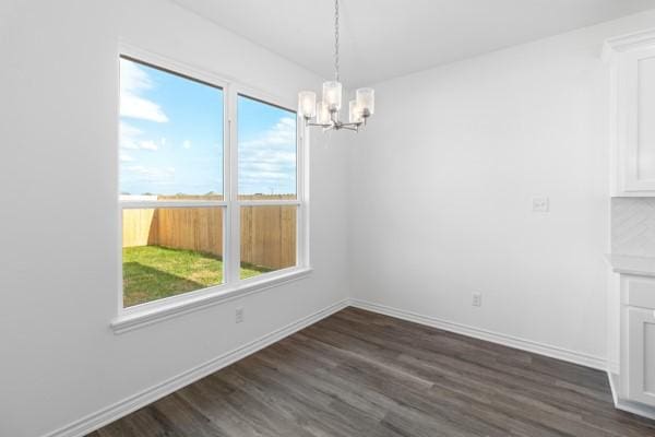 unfurnished dining area featuring plenty of natural light, baseboards, dark wood-type flooring, and a chandelier