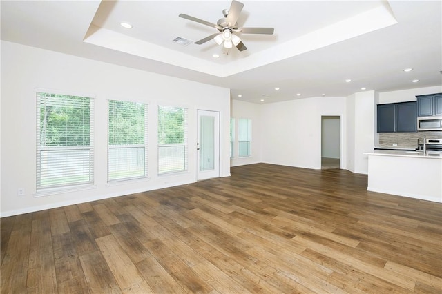 unfurnished living room with ceiling fan, dark hardwood / wood-style floors, and a raised ceiling