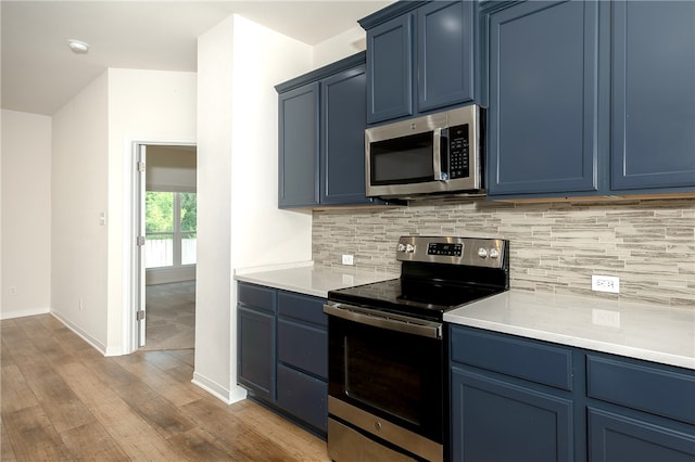 kitchen with light wood-type flooring, stainless steel appliances, blue cabinetry, and backsplash