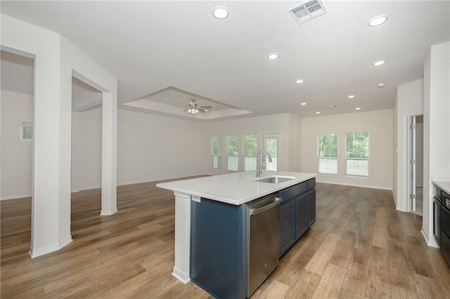 kitchen featuring stainless steel dishwasher, sink, light wood-type flooring, blue cabinets, and a center island with sink