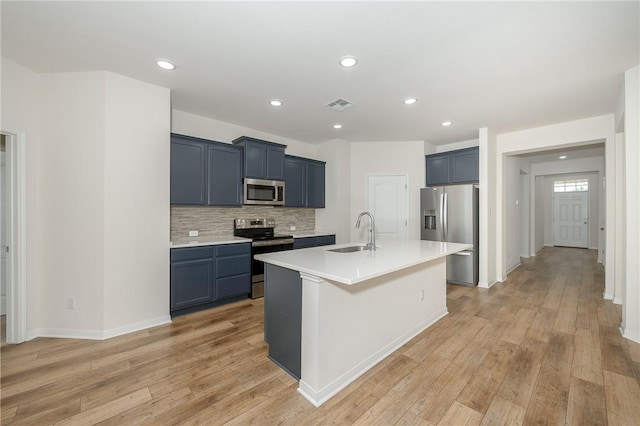 kitchen with light hardwood / wood-style floors, sink, appliances with stainless steel finishes, and an island with sink