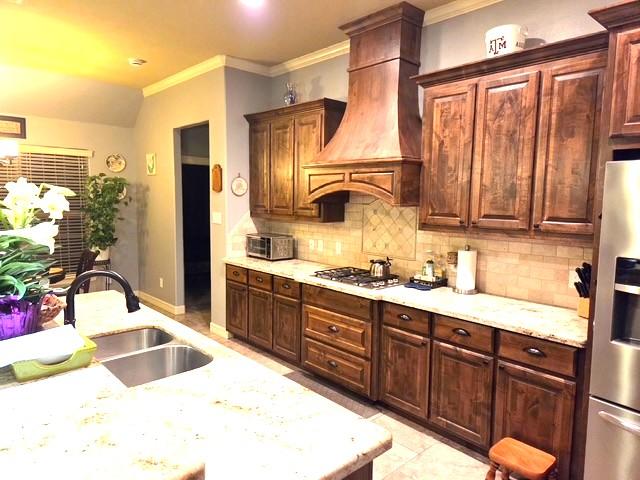 7585 Field Creek Estates Dr, Bryan, TX 77808 - kitchen with stainless steel appliances, a sink, crown molding, custom exhaust hood, and backsplash
