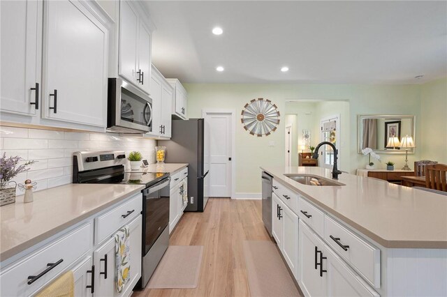 3914 Alamosa St, College Station, TX 77845 - kitchen with stainless steel appliances, a sink, light wood finished floors, white cabinetry, and backsplash