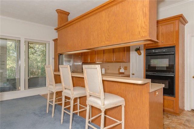 kitchen featuring double oven, stainless steel fridge, crown molding, and a kitchen breakfast bar