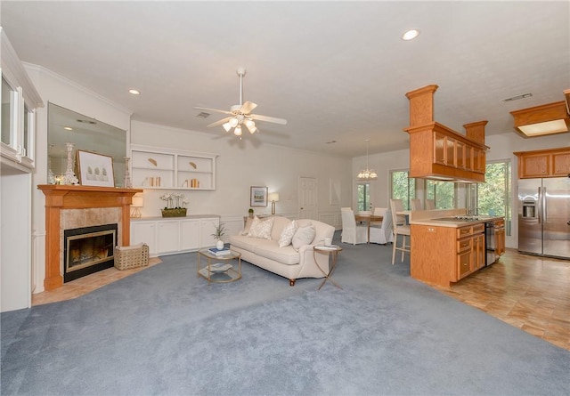 living room featuring ceiling fan, light colored carpet, crown molding, and a tiled fireplace