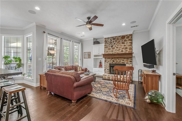 living area featuring a stone fireplace, dark wood-style floors, a ceiling fan, and crown molding