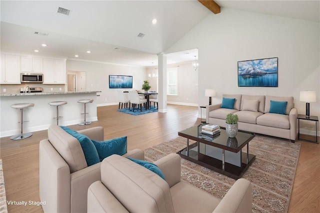 living area featuring lofted ceiling with beams, an inviting chandelier, light wood-style flooring, and visible vents