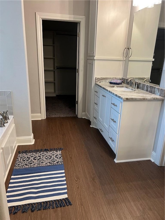 bathroom with wood finished floors, vanity, baseboards, a spacious closet, and a bath