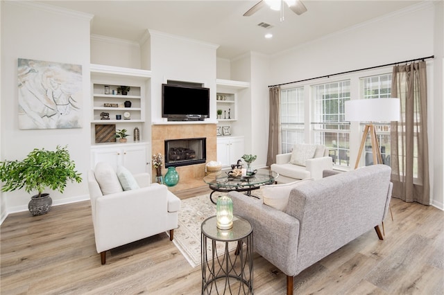 living room featuring visible vents, ornamental molding, a fireplace, light wood-style floors, and ceiling fan