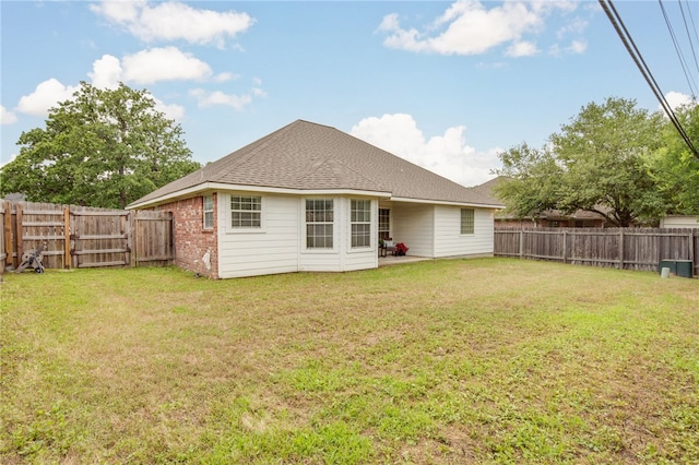 rear view of property featuring a fenced backyard, a patio area, roof with shingles, and a yard