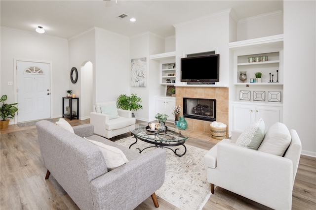 living area with crown molding, arched walkways, built in features, and wood finished floors