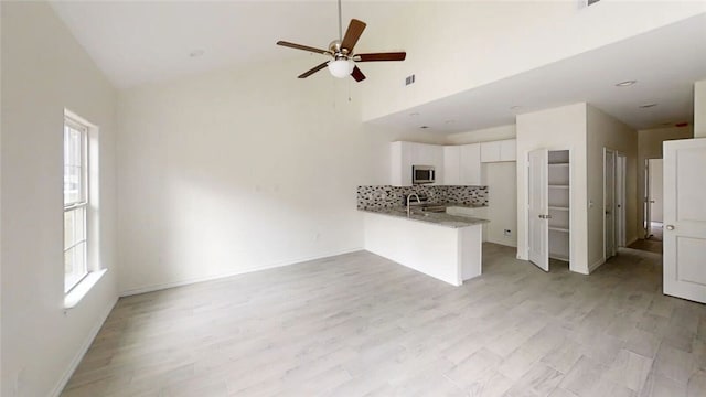 unfurnished living room with ceiling fan, sink, a high ceiling, and light wood-type flooring