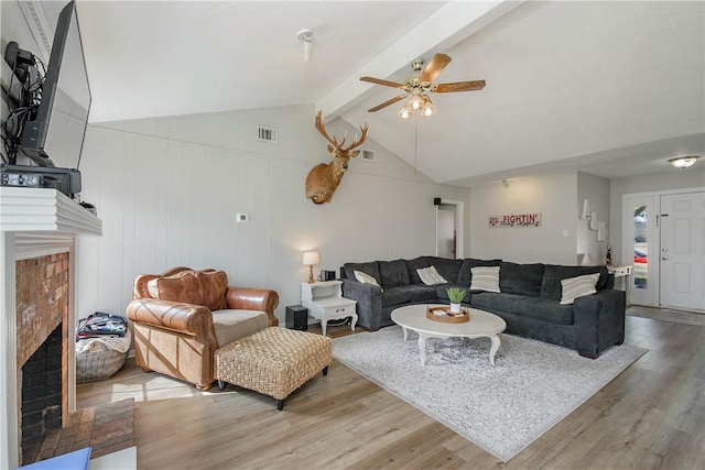 living room with ceiling fan, vaulted ceiling with beams, hardwood / wood-style floors, and a fireplace