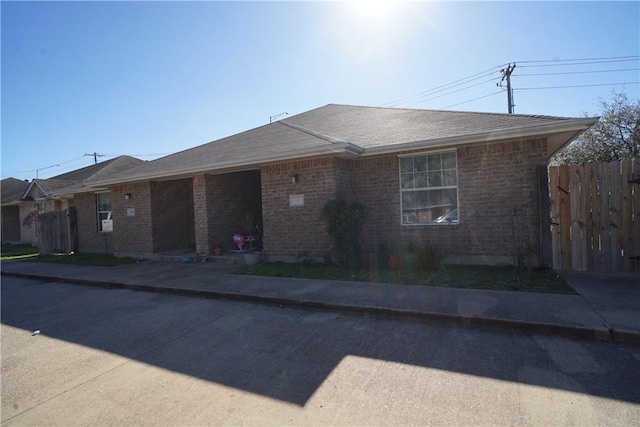 ranch-style home with brick siding, roof with shingles, and fence