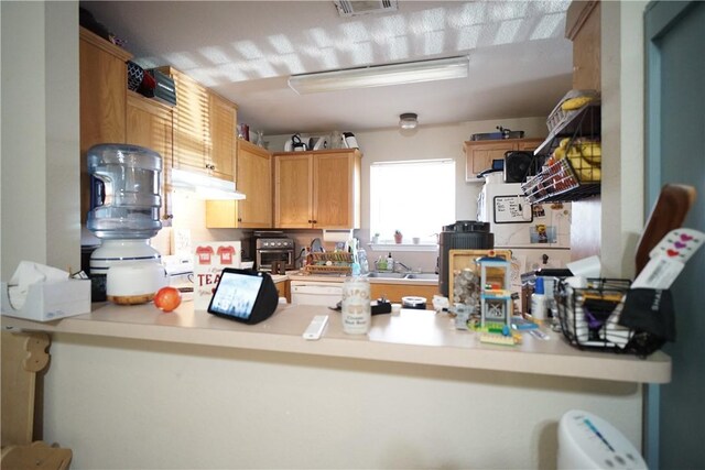 kitchen with a peninsula, under cabinet range hood, visible vents, and light countertops