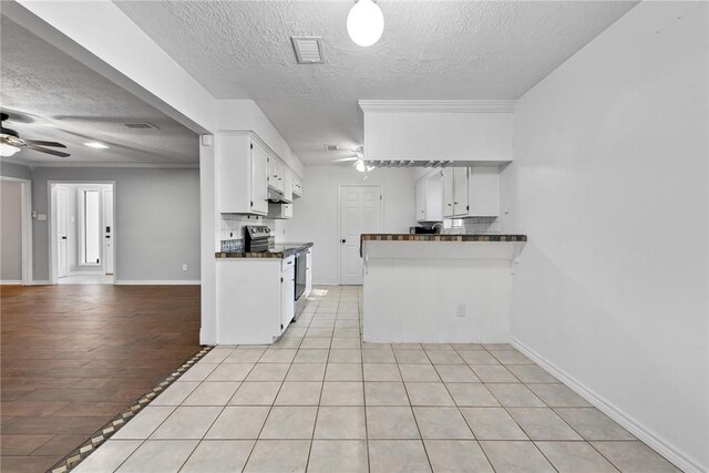 kitchen featuring ceiling fan, light tile patterned flooring, stainless steel range with electric cooktop, backsplash, and white cabinets