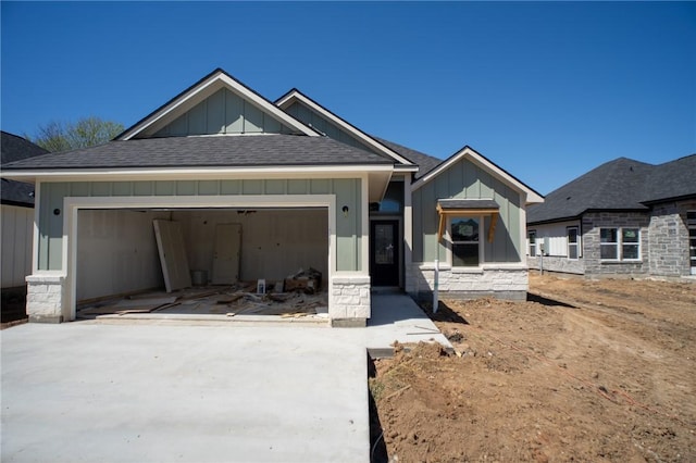 2581 Dove Xing, Navasota, TX 77868 - view of front of home featuring stone siding, a garage, concrete driveway, board and batten siding, and a shingled roof