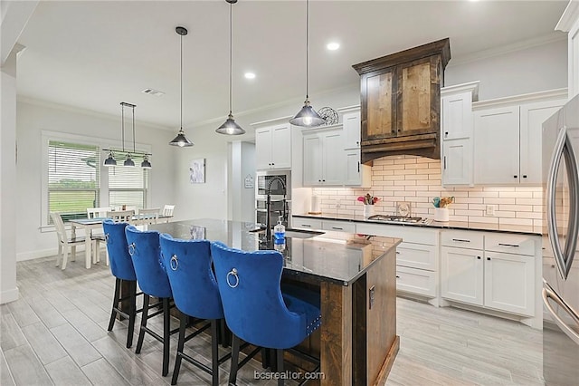 kitchen with white cabinetry, a center island with sink, hanging light fixtures, and ornamental molding