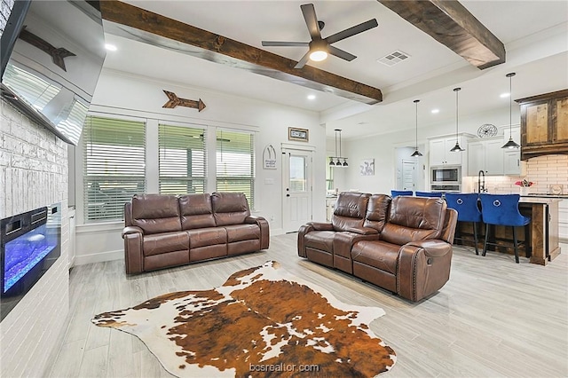 living room with light wood-type flooring, a fireplace, ceiling fan, crown molding, and beamed ceiling