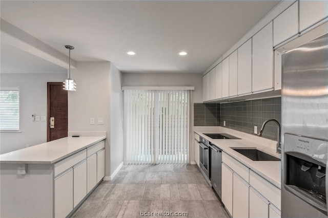 kitchen with white cabinets, sink, tasteful backsplash, decorative light fixtures, and stainless steel appliances