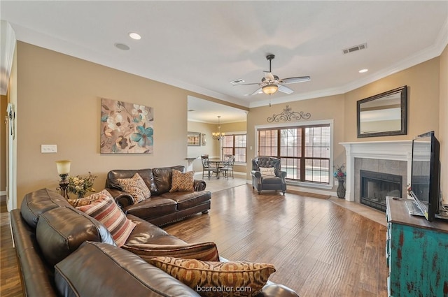 living room featuring hardwood / wood-style flooring, ornamental molding, ceiling fan with notable chandelier, and a tile fireplace