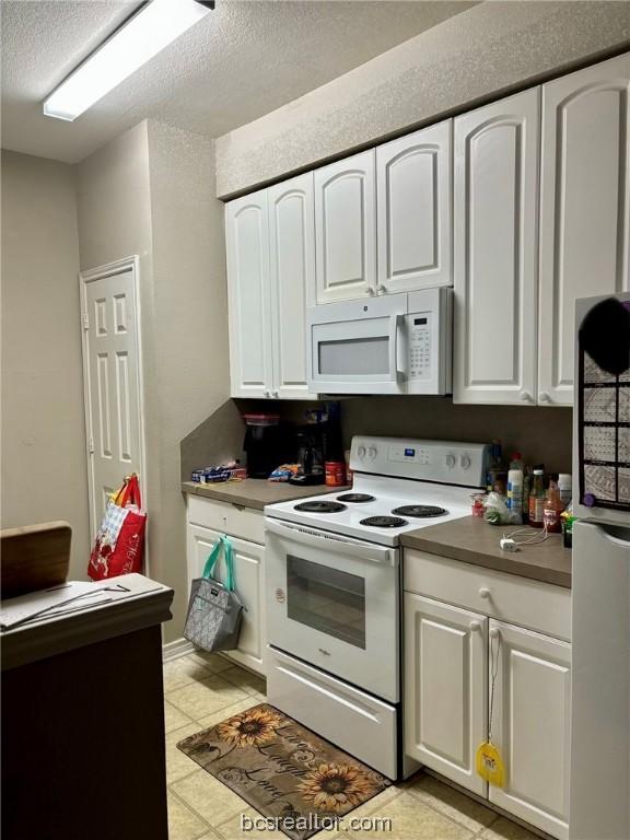 kitchen featuring a textured ceiling, white cabinets, light tile patterned flooring, and white appliances