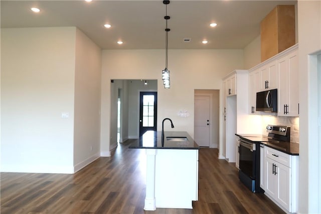 1977 Cambria Dr, Bryan, TX 77807 - kitchen featuring appliances with stainless steel finishes, dark countertops, white cabinetry, a kitchen island with sink, and recessed lighting